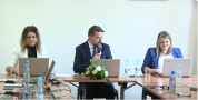 mężczyzna i po bokach siędzą dwie kobiety. Na stolikach stoją laptopy.