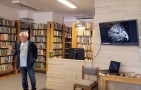 mężczyzna stoi w bobliotece. Na telewizorze wyświetlana jest głowa praka