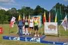 trzech zawodników stoi z trenerem na podium