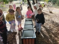  dzieci stojące obok parkowych koszów na śmieci i segregujące zebrane śmieci.