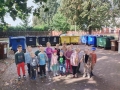 cześć uczestników akcji pozujących do zdjęcia grupowego. W tle znajdują się duże osiedlowe kosze na śmieci.