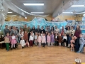 Dzieci, rodzice oraz organizatorzy pozują do wspólnego zdjęcia. W tle zimowa dekoracja.