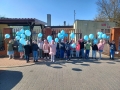 Dzieci stoją przed przedszkolem, w ręku trzymają niebieskie balony