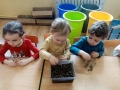 troje dzieci siedzi przy stoliku i wkłada do słoików produkty
