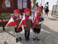 zuchy ubrane w zielone koszulki z napisem Przedszkole nr 1 w Hajnówce, na głowie mają czerwone berety, a w ręku flagi Polski.