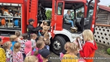 dzieci siedzą w wozie strażackim. Przed wozem ustawiona kolejka dzieci