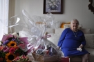 jubilatka siedzi na kanapie, na toliku leżą kwiaty i stoi kosz ze słodyczami