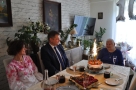 przy stole siedzi Jubilatka burmistrz i pani kierownik USC. Na stole stoi tort z paląca się świecą.