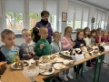 Dzieci, nauczycielki i pani leśnik stoją przy dużym stole, na którym wyeksponowane są różne gatunki grzybów.
