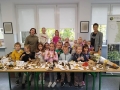 Dzieci, nauczycielki i pani leśnik stoją przy dużym stole, na którym wyeksponowane są różne gatunki grzybów.