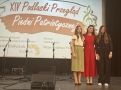 trzy młode kobiety stoją na scenie. W tle wyświetlany tytuł konkursu