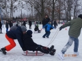 konkurencje na lodzie w trójkach. Jedno dziecko siedzi na sankach, inne dzieci ciągną i pchają sanki.