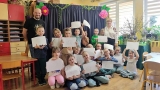grupa dzieci pokazuje swoje prace. Obok stoi opiekunka i prowadzący zajęcia